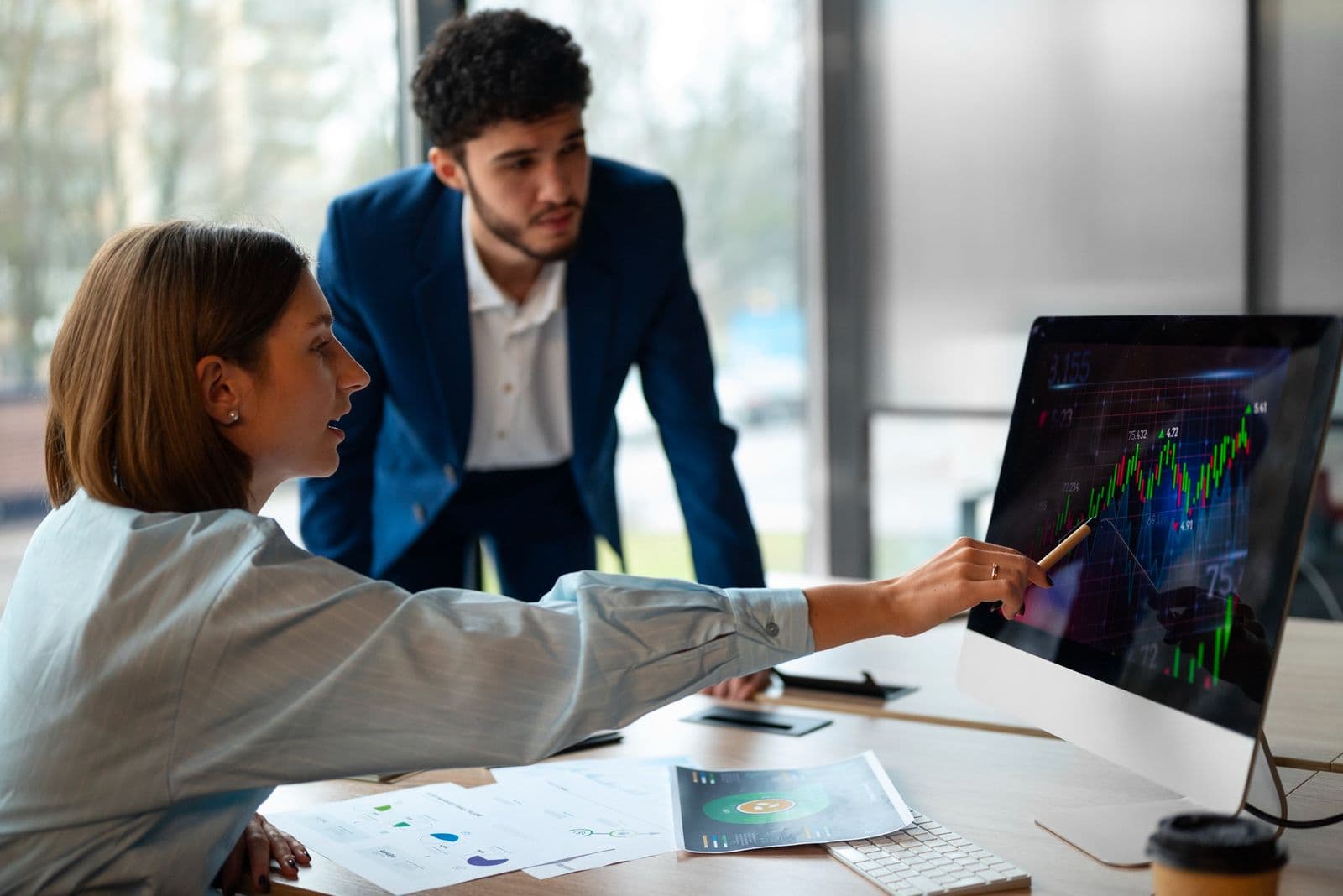 Two financial analysts collaborating at a computer screen to evaluate live candlestick chart patterns and market performance metrics.
